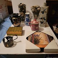 All items arranged on table: glass vases with stones, porcelain vases, teapot, lidded box, candle holder, framed print