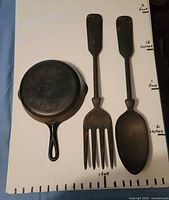 Top view of skillet base, fork, and spoon on measurement board