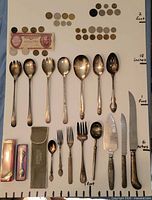 All flatware, souvenir spoons in boxes, coins, banknote laid out with scale