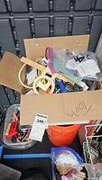 overview of cardboard box atop bucket with mixed hardware and electrical items