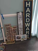 Overall lot showing tall "HARDWARE" sign, welcome board, metal slat signs, canvas prints and register cover