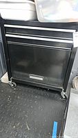 Front view of black metal tool chest showing two drawers, silver trim, and casters