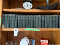 Full shelf view of approximately 25 uniform dark green cloth Dickens volumes; wear visible on some spines