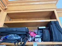 Overall view showing multiple bags, pink headphones, cables and boxed 3D pen on shelf
