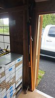 Two Fiskars pole saws leaning against wall showing full length
