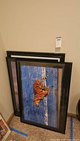 Stacked framed art pieces leaning against wall showing tiger print in black frame