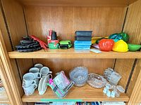 Overall lot on two shelves showing glassware, mugs, trivets, plastic items