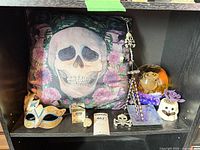 All seven items displayed on shelf: pillow, mask, trinket box, pendant, wind chime, rose paperweight, ceramic skull figurine