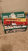 Red Hess fire truck with yellow ladder resting on green Hess Dump Truck and Loader boxed set