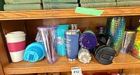 Mixed insulated and plastic tumblers on shelf showing variety of colors and materials