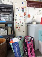 Tall white metal cabinet door covered with assorted magnets; two woven plastic shopping bags on floor
