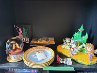 All items on shelf: snow globe, stacked plates, leg ornament, figurine diorama, Wicked plaque
