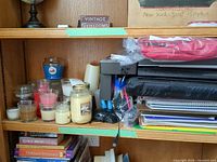 Shelf with jar candles, flameless candle, printer, office supplies visible
