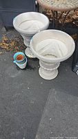 Two concrete urn planters beside stack of small plastic and terracotta pots