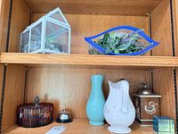 Shelf with terrarium, art glass bowl, amber dish, bell, turquoise vase, white pitcher, wood coffee grinder, plaque