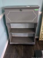 full front view of gray painted MDF cabinet with flip-down door and two shelves