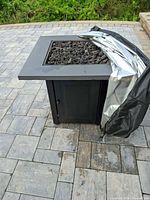 Full view of square metal fire pit with lava rocks and cover