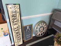 General Store sign, eye chart print and round wall clock leaning against wall