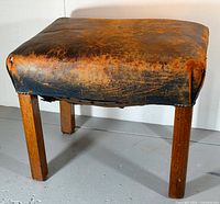 Full view of ottoman showing worn leather top and wood legs