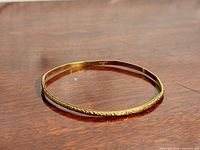 Full view of thin gold-filled etched bangle on wood surface