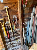 Overall wall showing soil tamper, weed puller, garden fork, lawn edger, bungee cords, lopper, metal poles