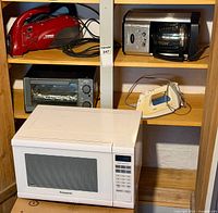 Shelving unit with red handheld vacuum, stainless coffee maker, toaster oven and Panasonic microwave