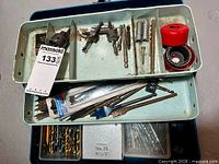 Open blue steel toolbox showing tray full of assorted drill bits, hole saw cutters and plastic bit cases