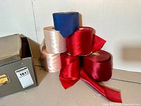 Stack of six wide ribbon rolls in red, pink and blue next to gray box