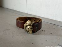 Leather belt rolled with brass skull cowboy hat buckle visible