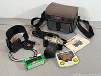 Lot overview showing all items together: Pentax camera, lens, bag, headphones, Tiger game, Fujicolor camera, manual