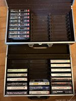Open hard carrying case showing blank cassettes, empty slots and lower tray with pre-recorded tapes