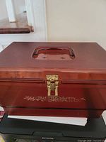 Closed amber sewing box showing handle, latch, floral decal