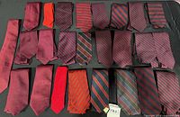 All 25 burgundy and red neckties laid out on flat surface showing variety of solid and striped designs