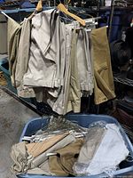 Multiple khaki pants hanging on wooden and plastic hangers above bin containing more pants and hangers