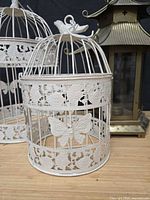 Front view of smaller white butterfly birdcage with larger cage and pagoda lantern partially visible