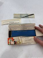 Open cardboard sleeve showing row of blue pencils and leaflets