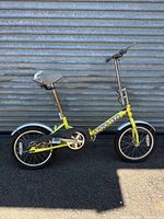 Full left-side view of yellow Titan folding bike against metal wall