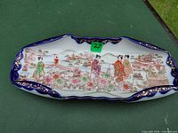 Full view of elongated porcelain dish showing overall shape, scalloped rim and painted scene