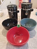 Two black clamp-lid jars and three coloured bowls displayed on tabletop