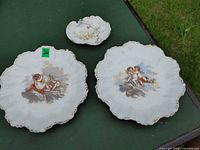 Overview of two cherub plates and floral handled dish on table