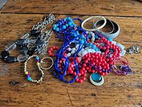 Group shot of assorted multicolour beaded necklaces, bracelets, bangles and charms on wooden surface