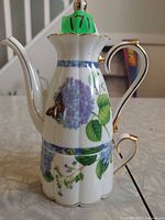 Side view of teapot showing floral and butterfly design with gold trim
