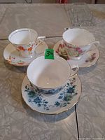 Three teacups on matching saucers showing floral patterns and gold trim