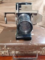 Front view of projector mounted on carrying case showing lens and slide gate