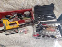 Overview of lot showing DeWalt stapler, crow bars, socket set, toolbox tray, hardware kit and wire basket of tools