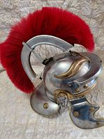 Left side profile showing steel body, brass-tone trim, cheek guard and full red plume