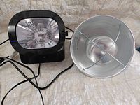 Front view of black strobe light and silver reflector flood fixture with cords
