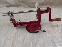 Overall side view of red Victorio apple peeler corer slicer showing hand crank, stainless rod, blades and suction base