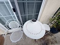 Overhead view of round white metal table with perforated design and two white metal mesh chairs