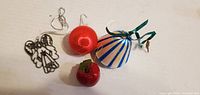 All four ornaments grouped: metal angel, red satin ball, red apple, bell shape white with blue stripes